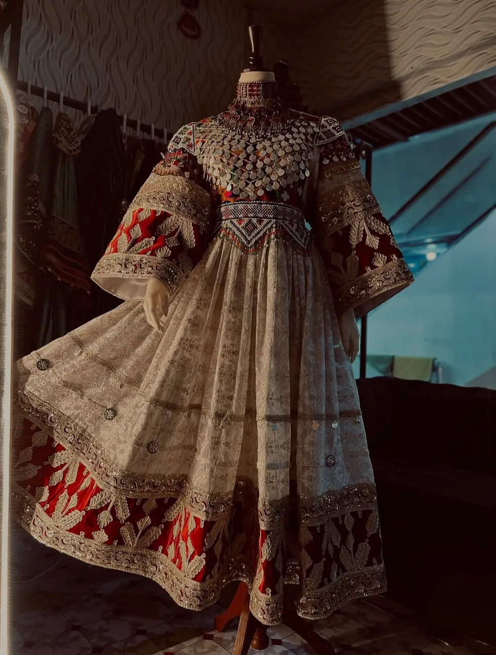 Traditional Afghan women's dress with silver embroidery and a red velvet border, displayed on a mannequin