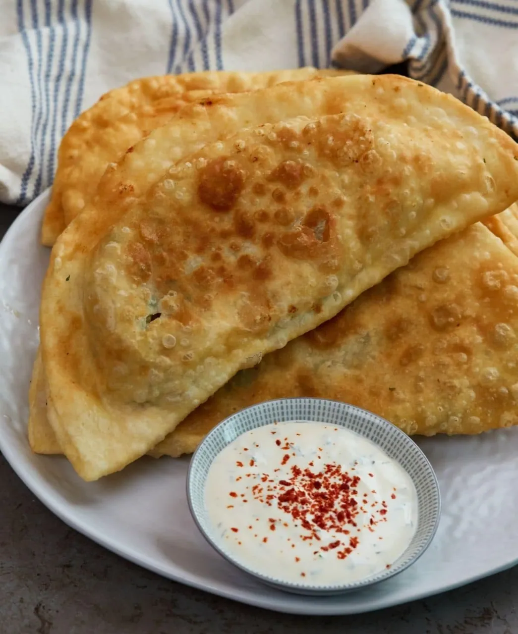 Pan-fried bolani flatbreads on a plate with a bowl of yoghurt dip