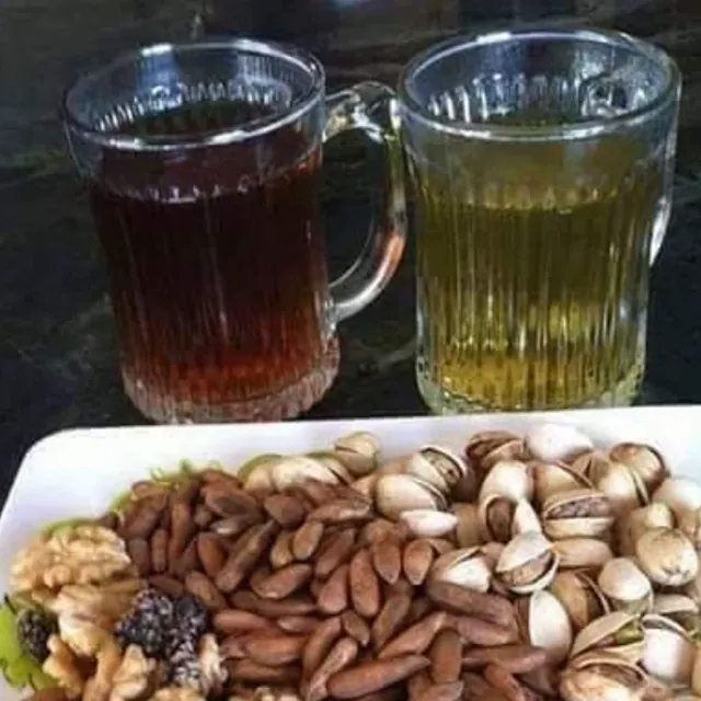 Two glass mugs of Afghan tea, one black and one green, beside a platter of nuts