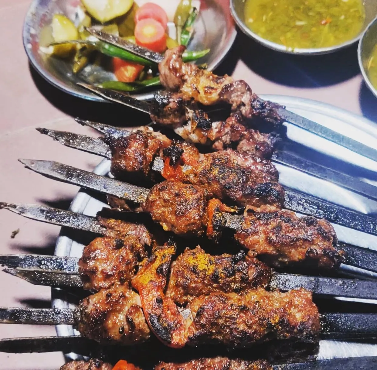 Charcoal-grilled kebab skewers on a metal tray with pickles and chutney