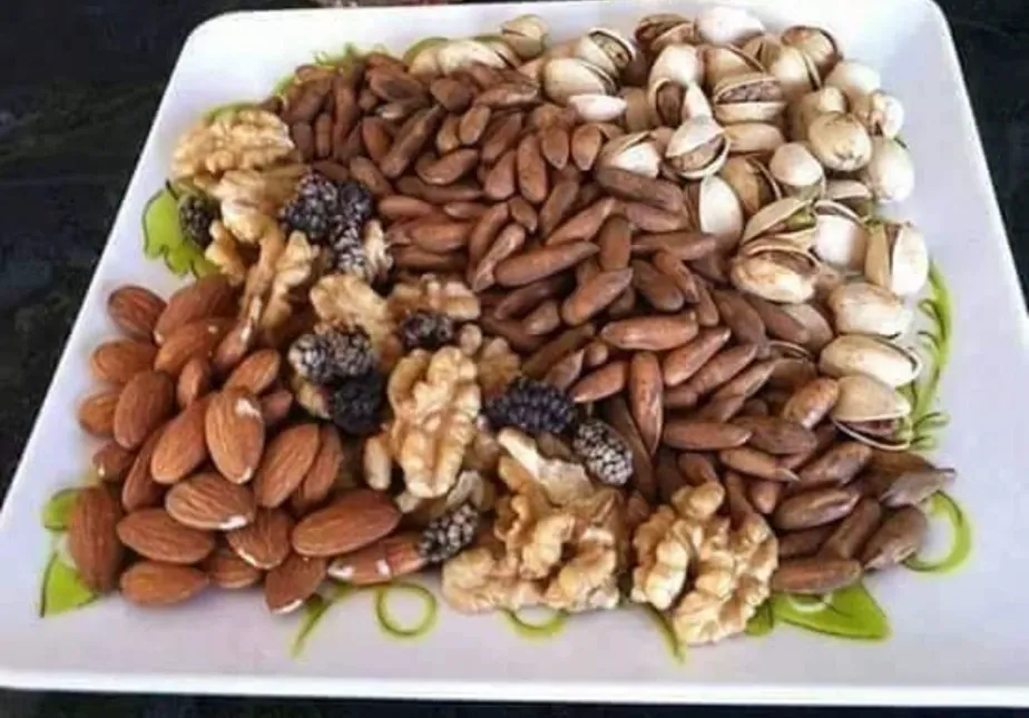 A white platter of almonds, pine nuts, pistachios, walnuts and dried mulberries