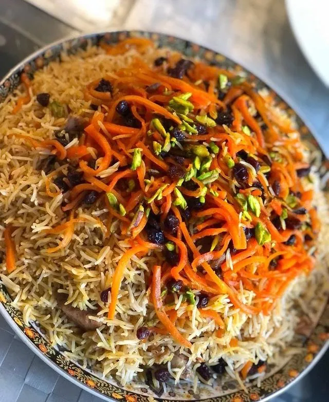 A platter of qabili palaw topped with julienned carrots, raisins and pistachios