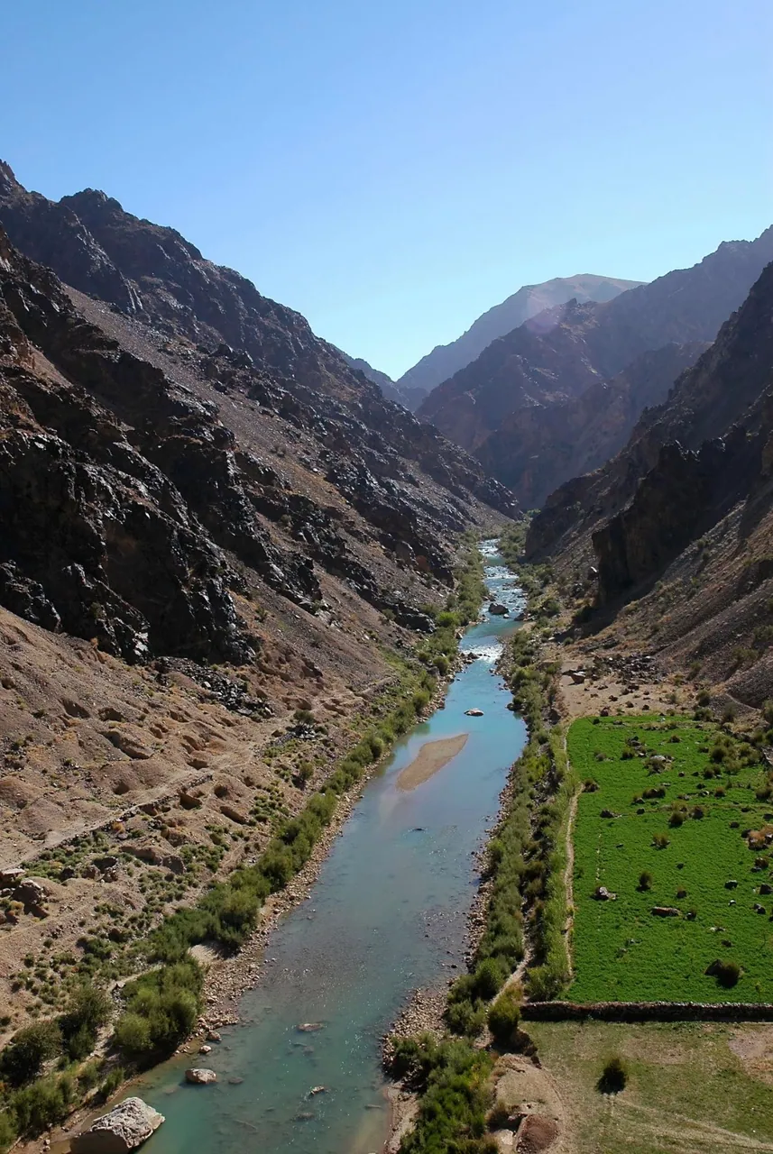 A river running through a steep, rocky gorge in Ghor, with a green field on one bank