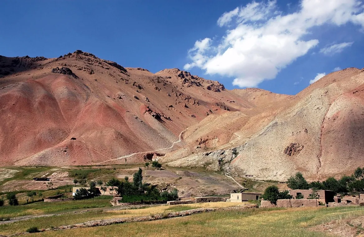 Red and grey hills above mud-brick houses and fields in Ghor, under a blue sky with white clouds