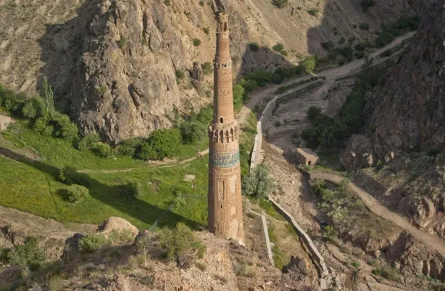 The Minaret of Jam seen from the hillside above, with green slopes and paths in the gorge around it