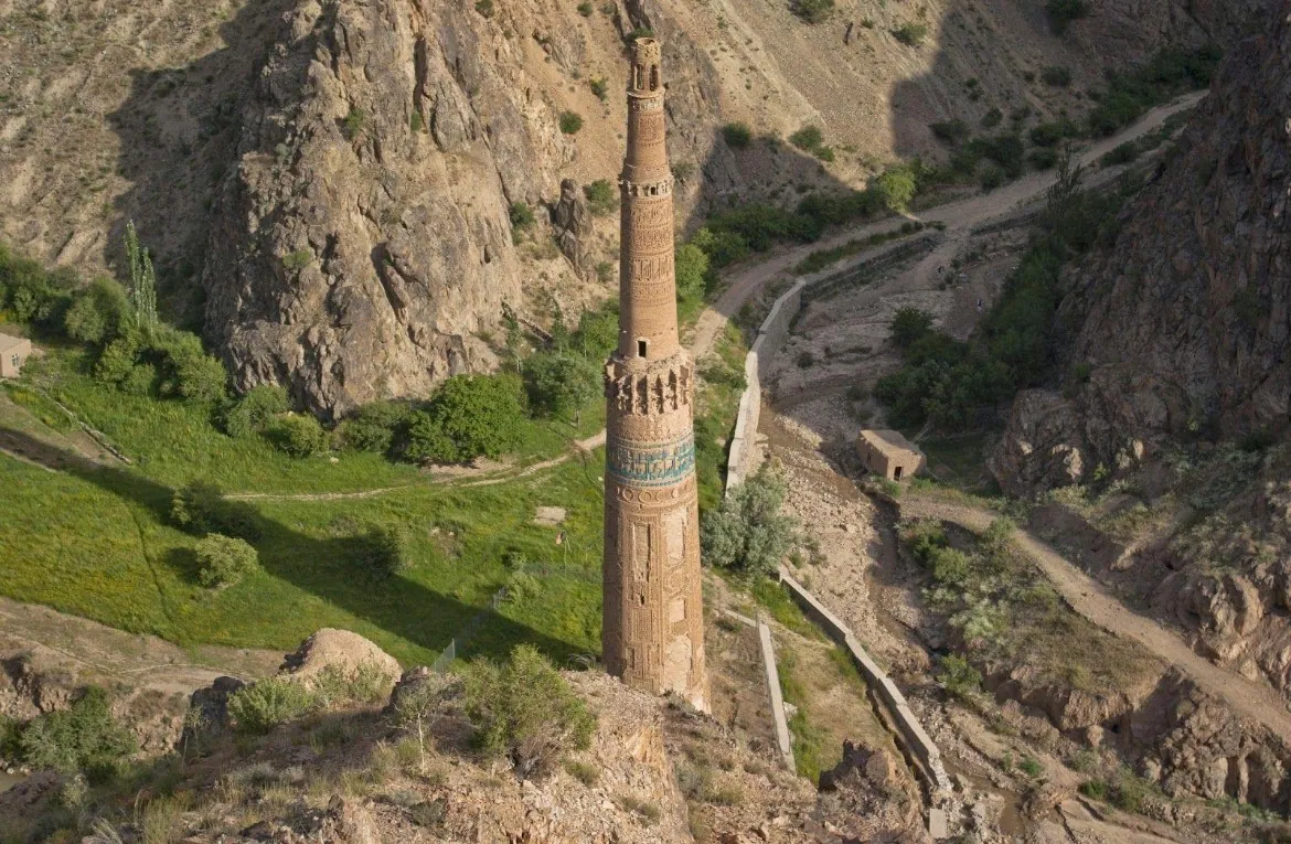 The Minaret of Jam seen from the hillside above, with green slopes and paths in the gorge around it
