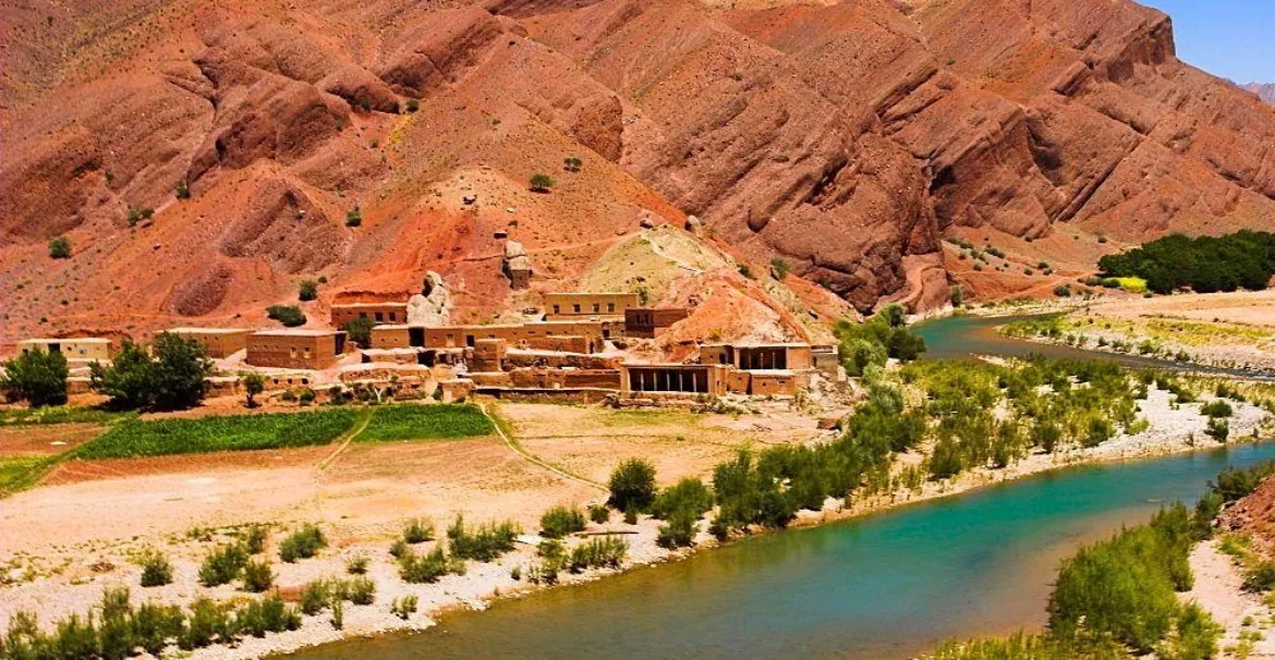 Mud-brick village beside a turquoise river below red mountains in Ghor