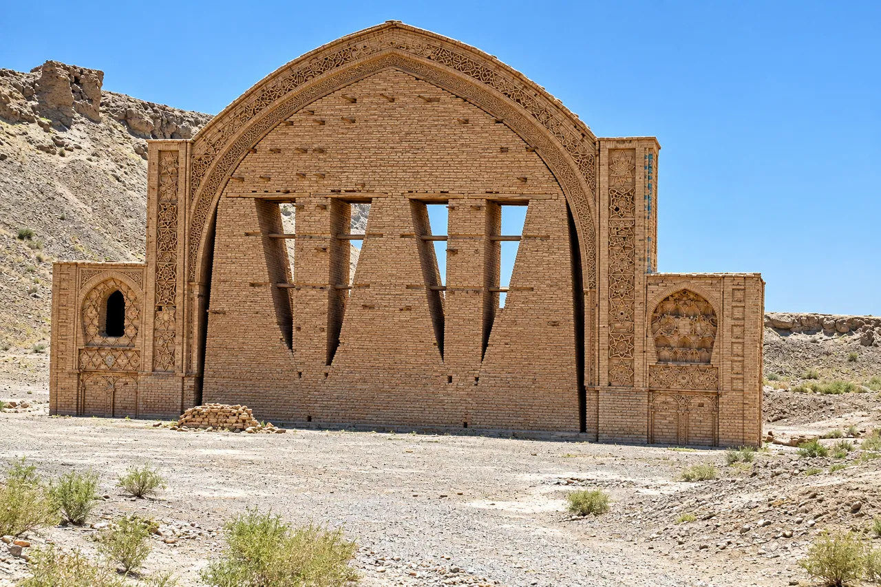 The brick arch of Qala-e Bost, a tall pointed arch with a decorated frame, standing on dry ground under a blue sky
