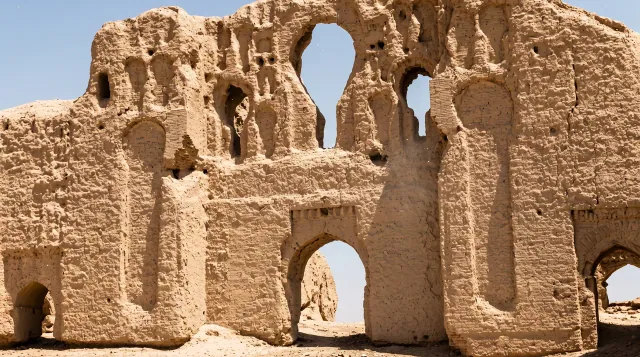 A tall eroded mud-brick wall with arched openings among the ruins of Lashkari Bazar
