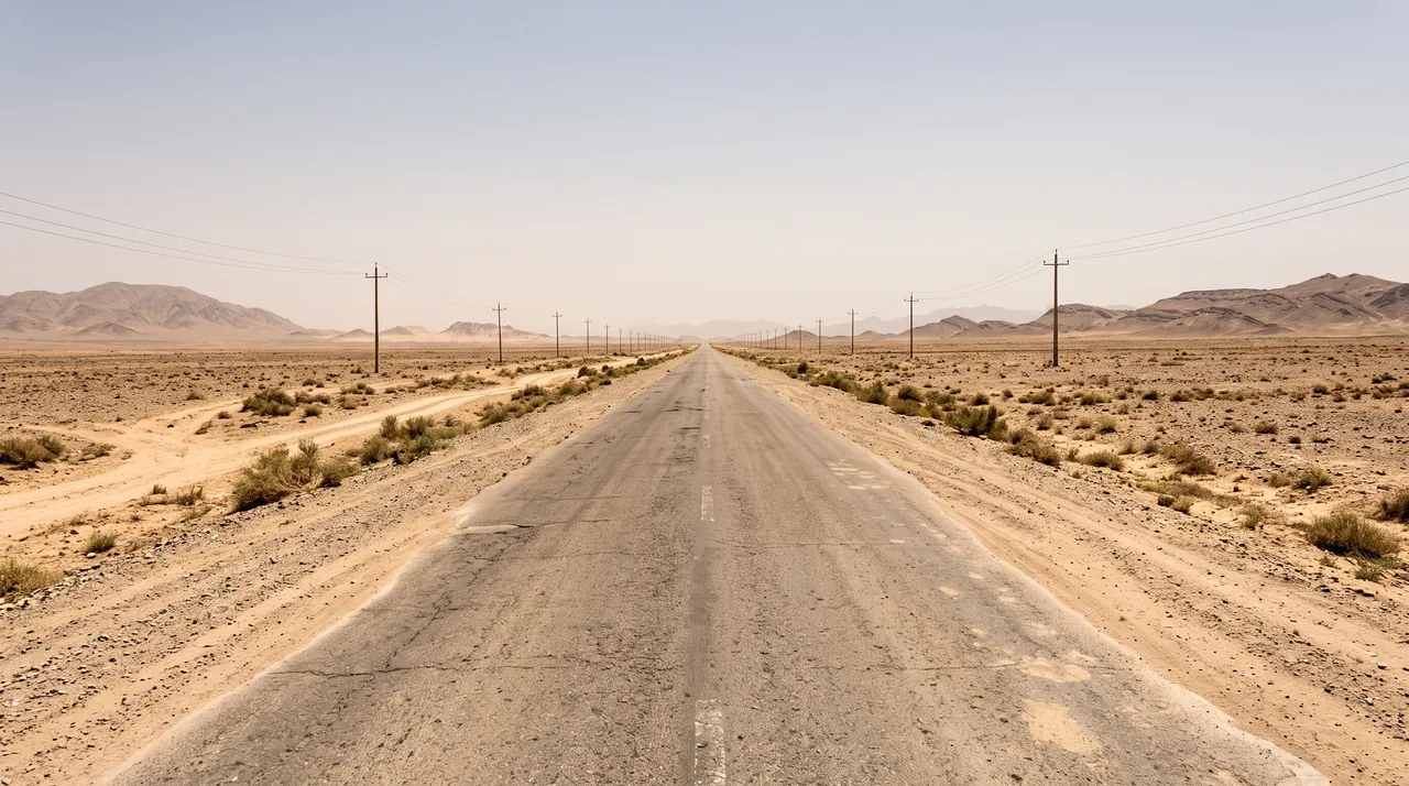 A straight paved road with power lines crossing the flat desert towards distant hills, on the way from Kandahar to Lashkar Gah