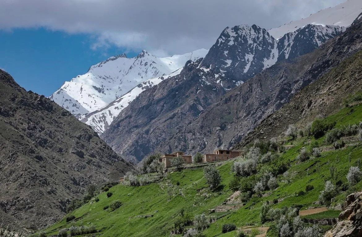 Snow-capped peaks above a green valley with mud-brick houses in Samangan