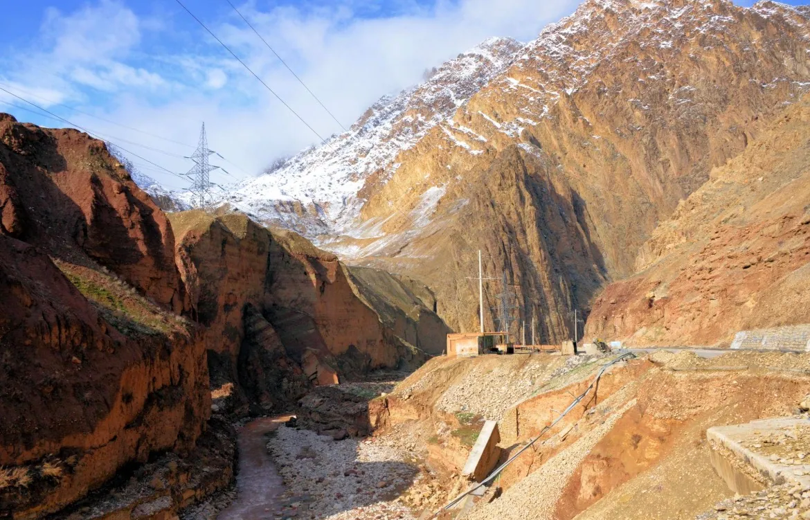 A rocky gorge with a road and power lines below snow-capped mountains in Samangan